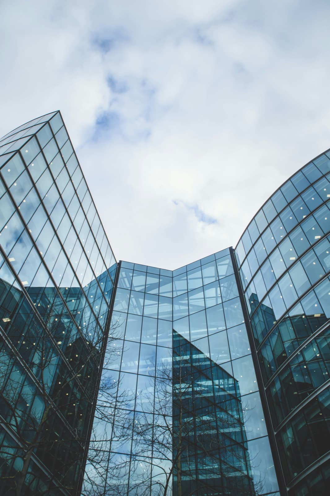 Curved glass office towers viewed from street level against a bright, clouded sky.
