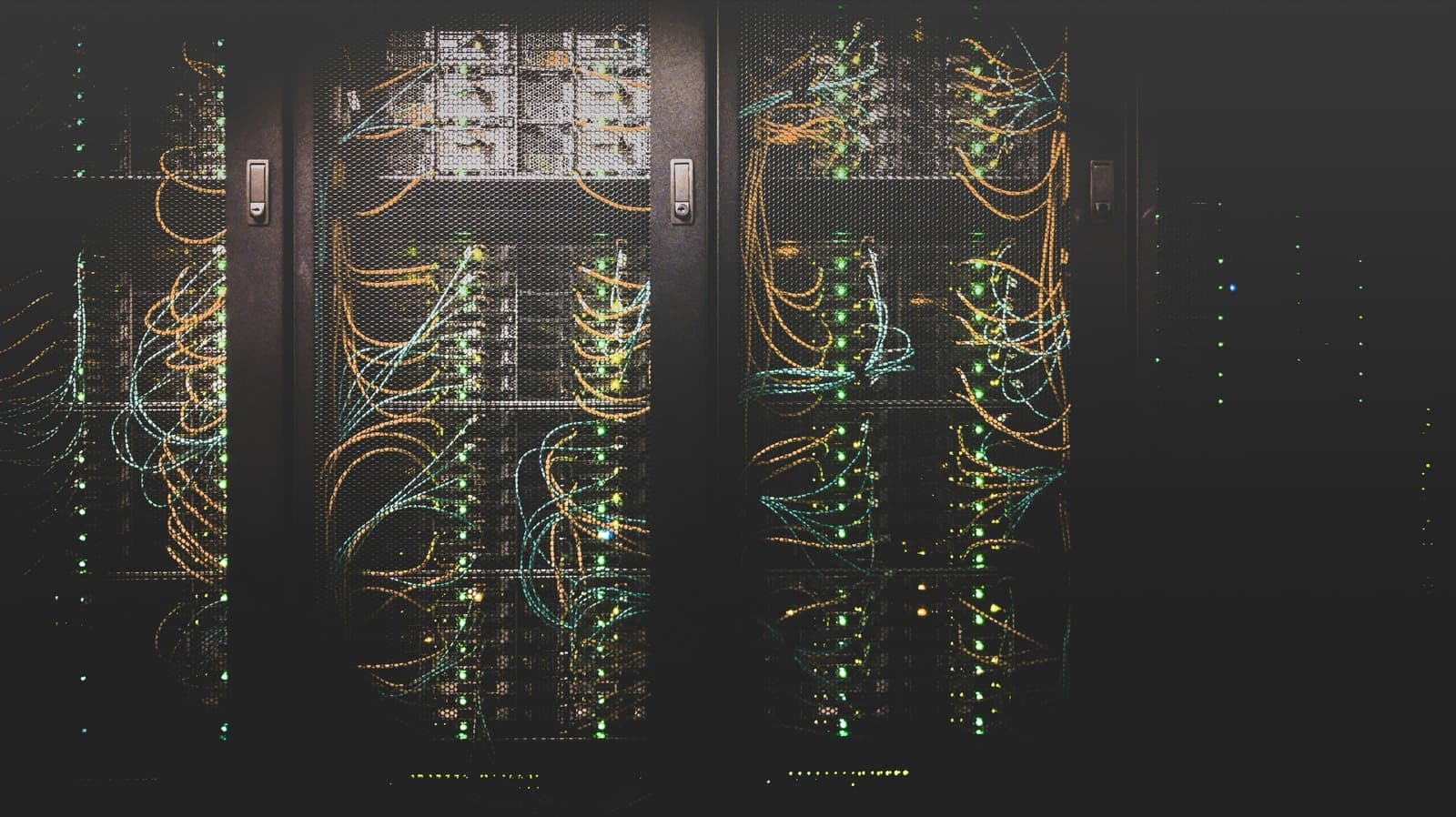 Racks of network equipment in a darkened data centre, threaded with lit fibre cabling.